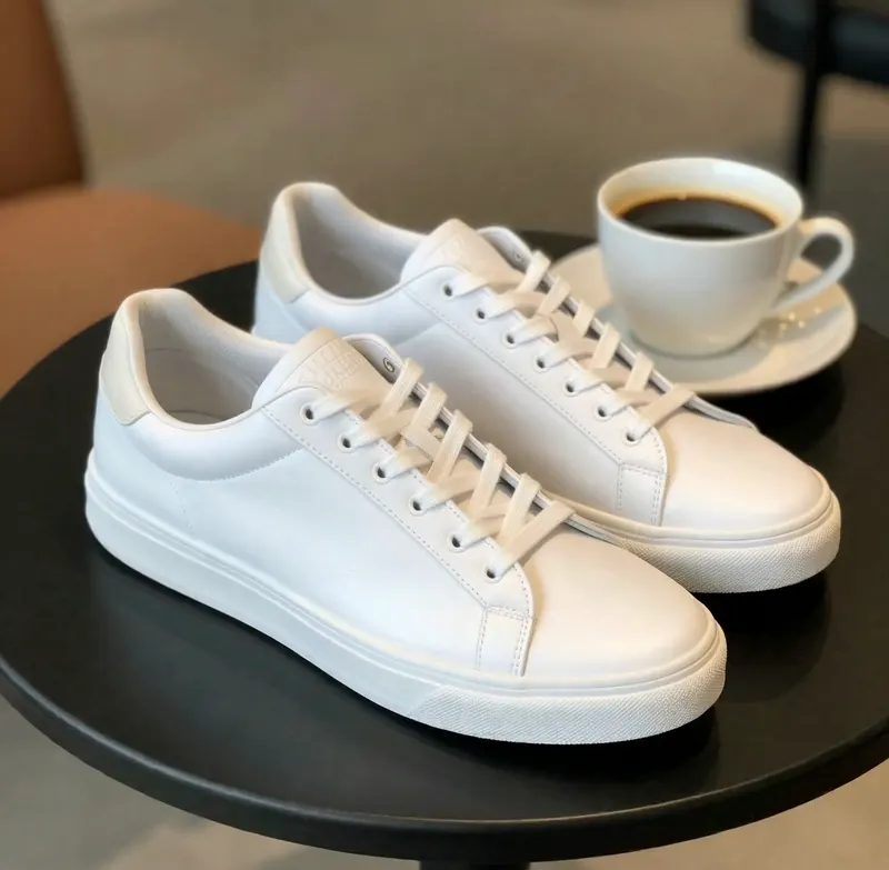Pair of white leather sneakers next to a cup of black coffee on a round cafe table