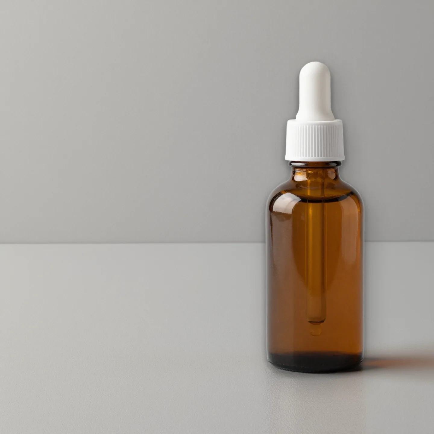 Amber dropper bottle on a clean grey studio background with space for a headline