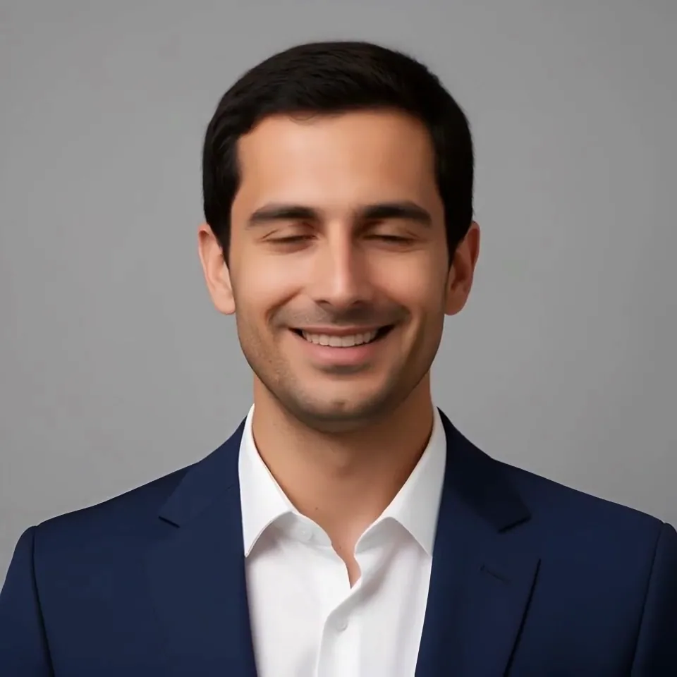 A smiling man in a navy suit and open white collar on a grey studio background