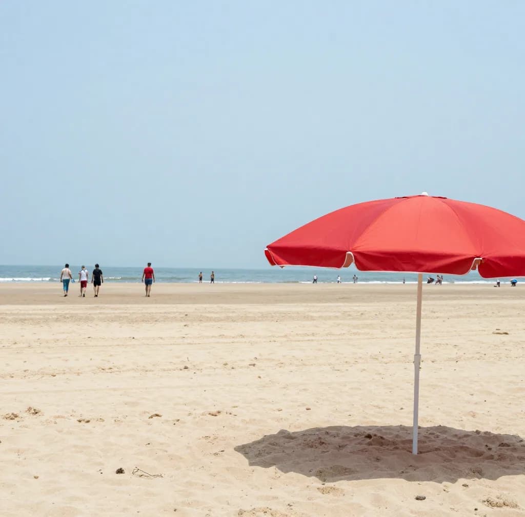 A red beach umbrella on a sandy beach with a few people in the distance